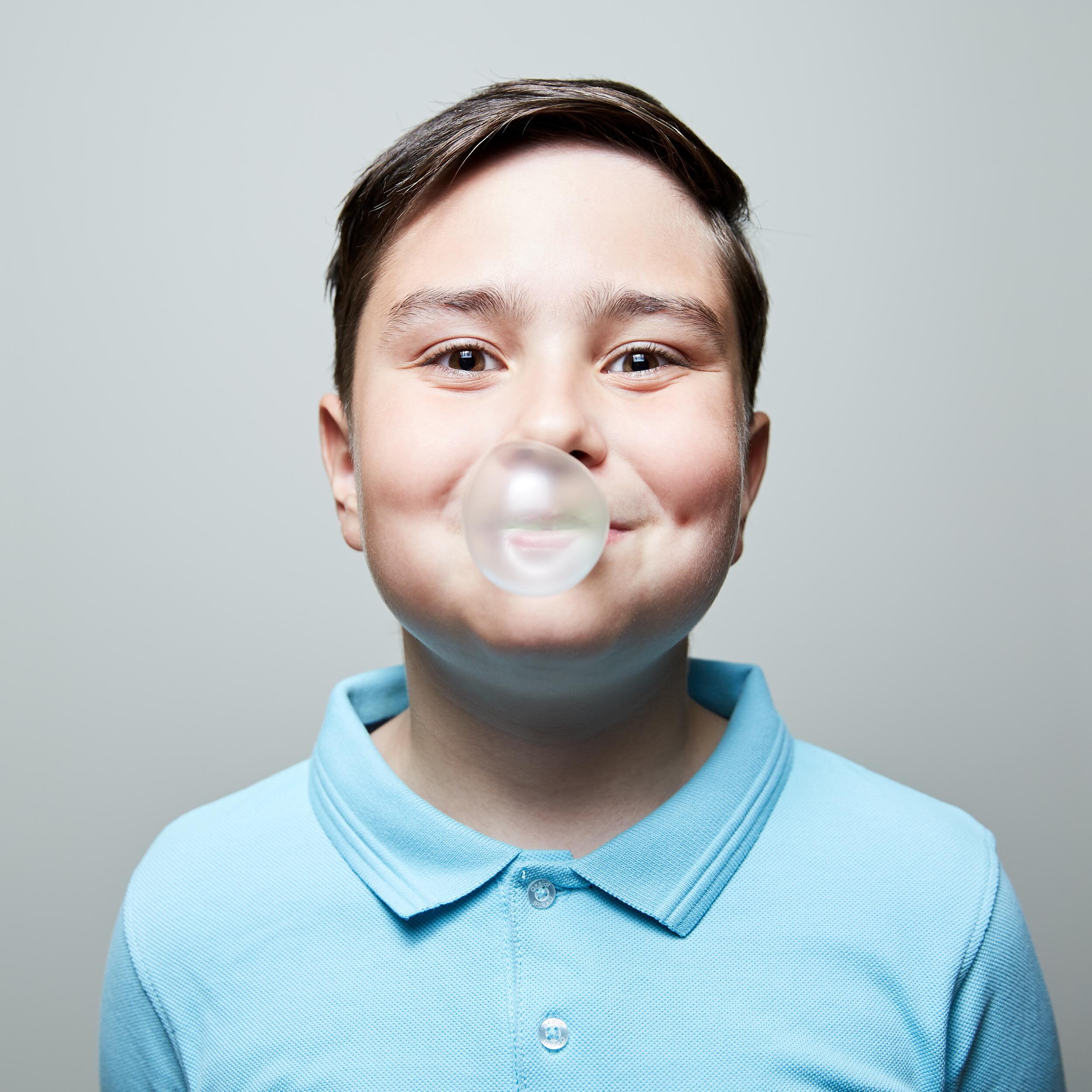 A boy in a blue shirt blowing a bubble gum.