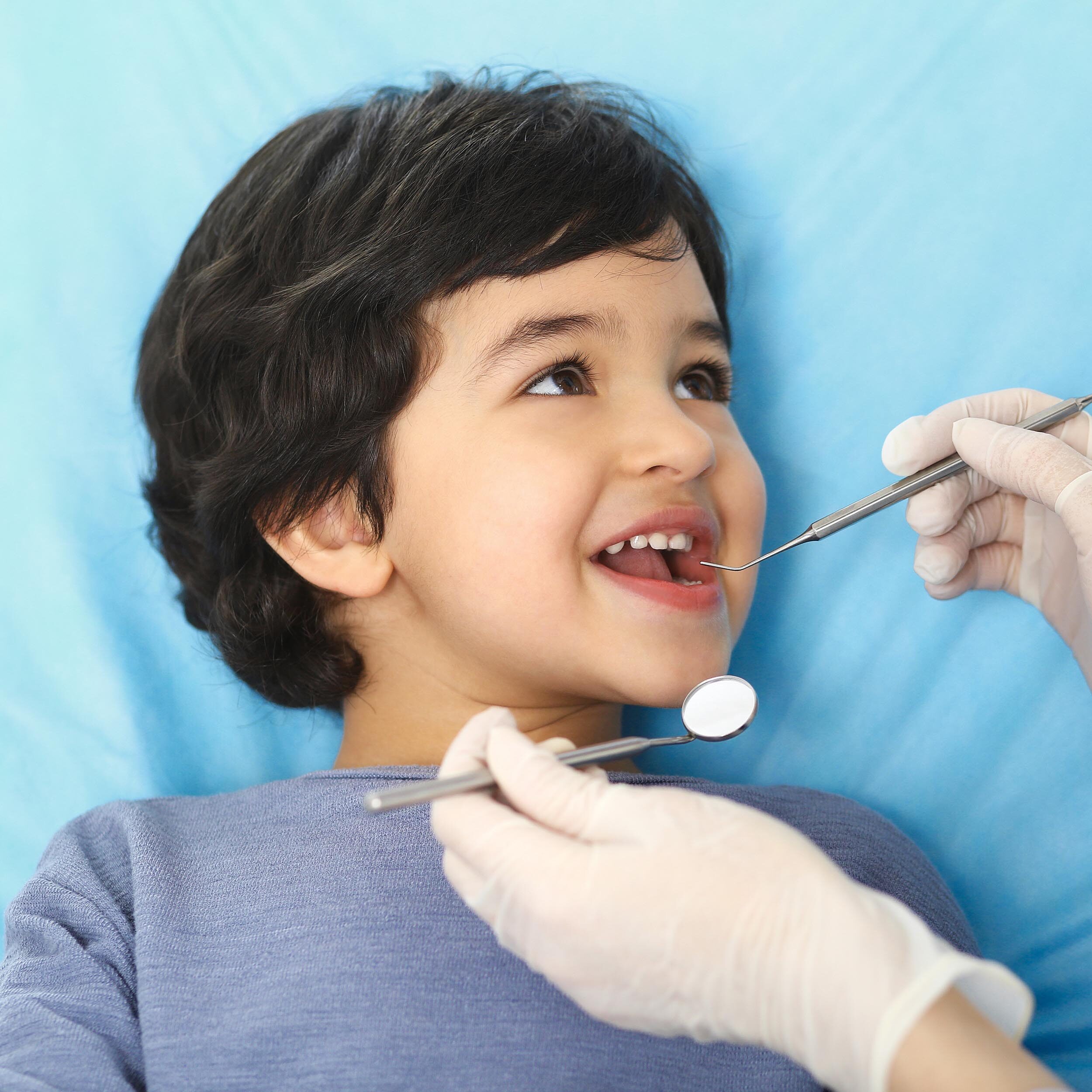 A child getting his teeth cleaned by a dentist, who is examining the boy's teeth for extraction.