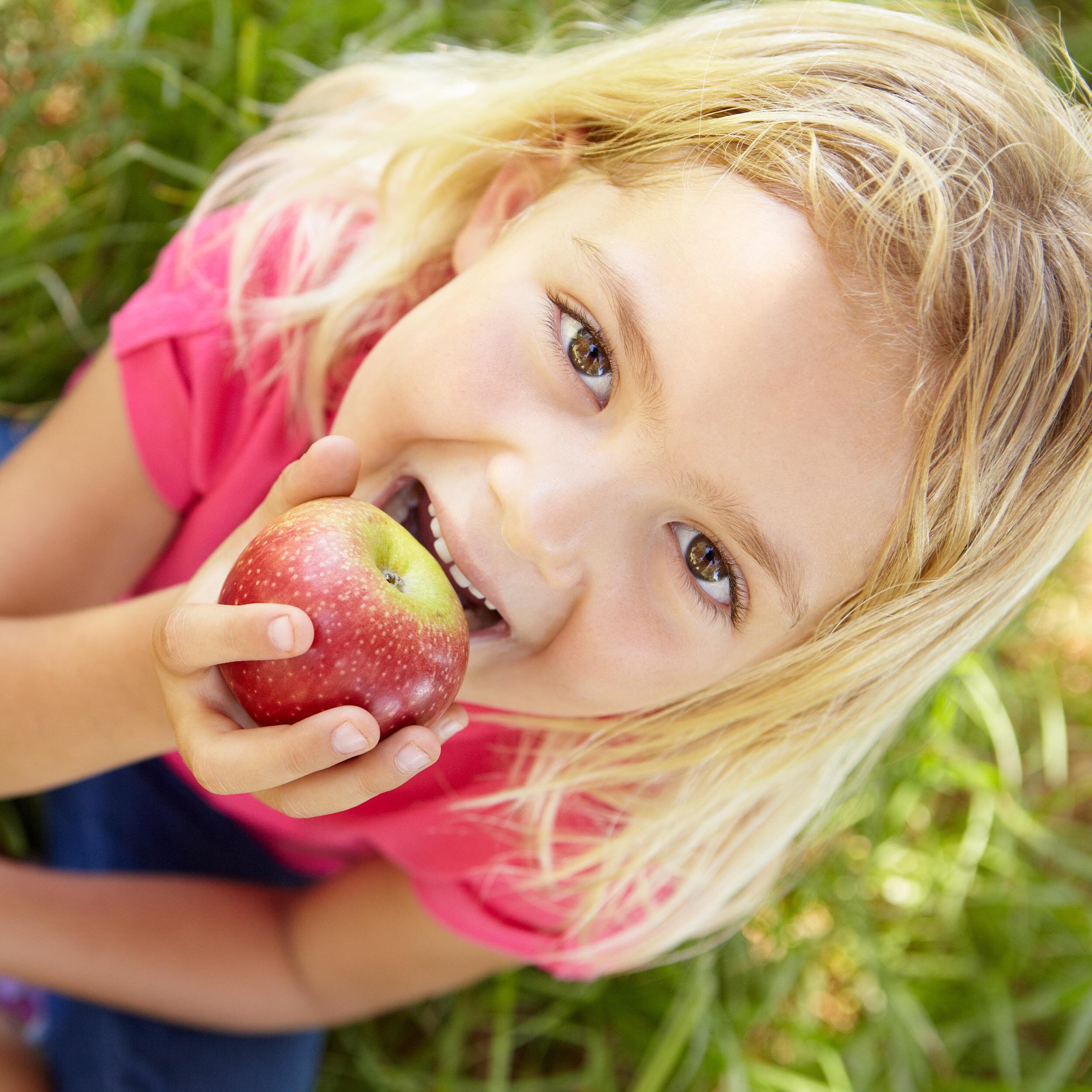 A young girl enjoying an apple while sitting in the grass.