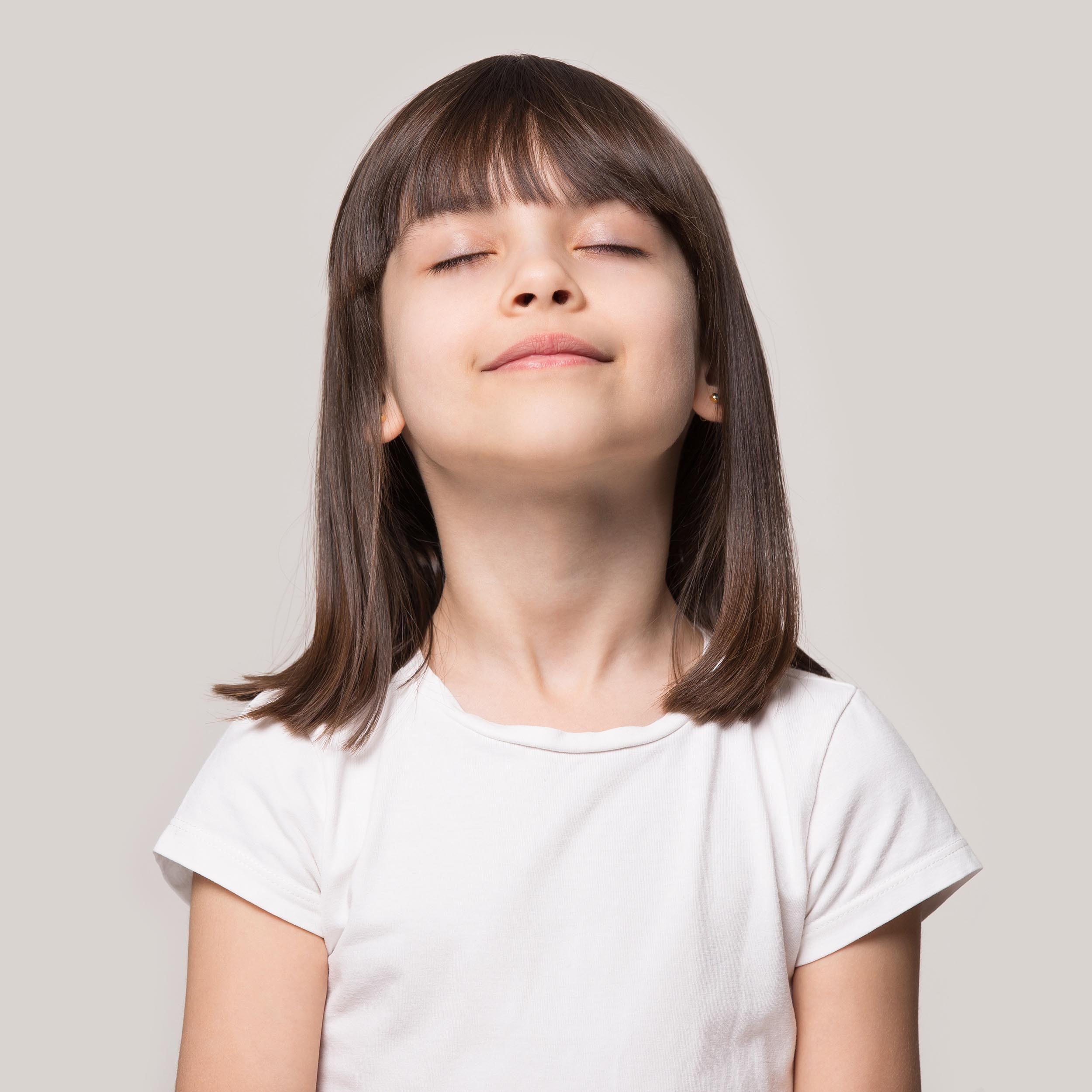 A little girl with closed eyes wearing a white shirt.