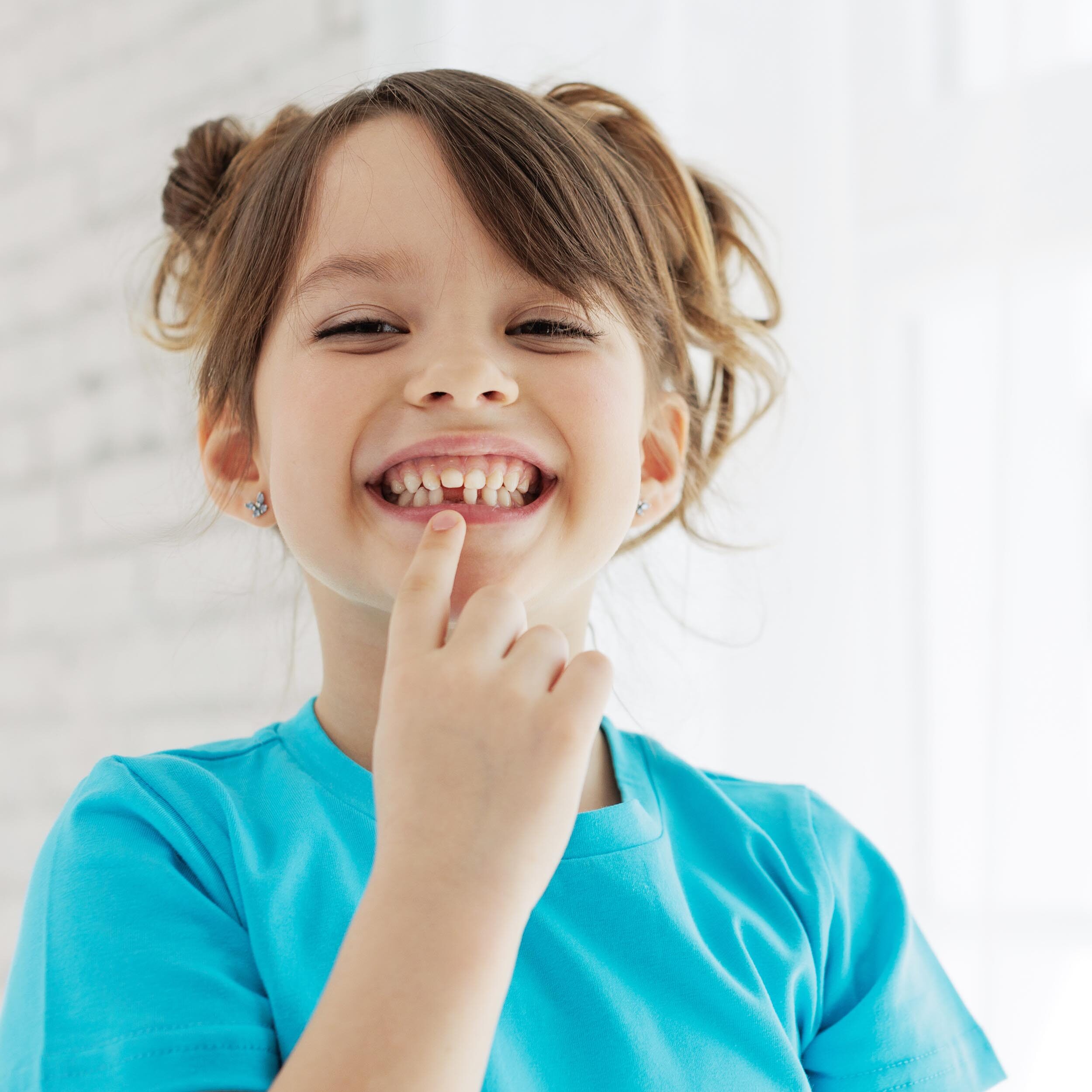 A smiling girl with her finger on her lips, displaying a space where her baby tooth once was, radiating joy.